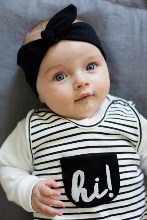 Liegendes süßes Baby Mädchen mit schwarz-weiß gestreiftem Baby Strampler mit Fuß & Tasche, weißem Oberteil, schwarzem Stirnband - Babystrampler von Pinokio - Babyphoto