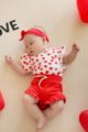 Liegendes Mädchen Baby trägt rote kurze Shorts Hose mit Rüschen & Kordel für den Sommer - Weiß rot gepunkteter Love Rüschen Wickelbody - Rotes Stirnband mit Schleife von Pinokio - Babyphoto