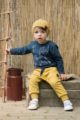Sitzender Junge trägt currygelbe Babyhose mit Taschen, Kordel & Patch - Blaues leichtes Baby Langarmshirt & gelbe Babymütze mit Füchse, Wald Blätter, Eicheln - Weiße Babyschuhe mit Klettverschluss von Pinokio - Babyphoto Kinderphoto