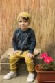 Sitzender Junge trägt gelbe Baby Pumphose mit Taschen - Dunkelblaues Babyshirt langarm & Baby Mütze mit Wald Blätter, Tiere, Füchse & Eicheln - Weiße Babyschuhe von Pinokio - Babyphoto Kinderphoto