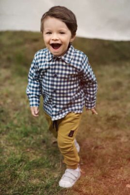 Staunender Junge trägt senfgelbe Baby Haremshose Pumphose mit Taschen, Kordel & Patch - Blau weiß kariertes Hemd Karohemd langarm - Weiße Babyschuhe mit Klettverschluss von Pinokio - Babyphoto Kinderphoto
