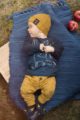 Liegender Junge trägt gelbe Baby Sweathose Leggings mit Füchse, Eulen & Eicheln - Marineblaues Langarmshirt Fuchs & Blätter - Currygelbe Babymütze mit Forest Patch - Blaue Fuchs Babyschuhe mit Ohren - Babyphoto