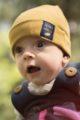 Junge trägt currygelbe Babymütze mit Umschlag & Patch SECRET FOREST - Blaue Latzhose mit Eichel - Weisser Wickelbody mit Fuchs, Uhus, Kauz von Pinokio - Babyphoto