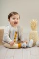 Lachender sitzender Junge trägt weißen Baby Wickelbody mit Papagei Motiv - Senfgelbe Streifen Leggings mit Schlupfbund - Plüschweste mit Reißverschluss Beige von Pinokio - Babyphoto