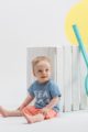Sitzender Junge trägt blaues kurzarm Babyshirt Kinder mit Sommer SEA Motiv - Korall Orange rote Shorts mit weißem Patch SUN & FUN von Pinokio - Kinderphoto Babyphoto