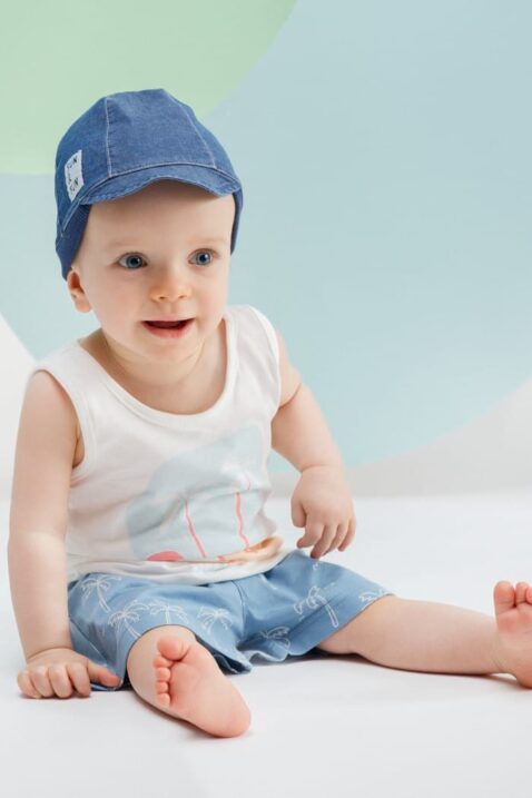 Sitzender staunender Junge trägt blaue kurze Hose mit Palmen - Tank Top ärmellos mit Insel, Meer & Sonne in Weiß - Baby Mütze mit Schirm & Patch in Dunkelblau von Pinokio - Babyphoto