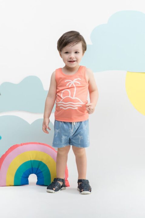 Stehender lachender Junge trägt Baby Kinder kurze Hose Shorts in Blau - Tank-Top mit Palme, Insel, Sonne in Koralle Orange Sommer von Pinokio - Kinderphoto Babyphoto