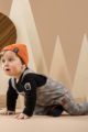 Krabbelnder Junge trägt Baby Latzhose Trägerhose in Tartan Southdown Grey - Body Polo schwarz mit Bär - Baby Mütze mit Umschlag in Orangebraun von Pinokio - Babyphoto