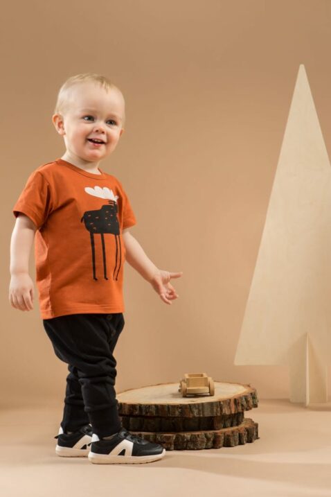 Stehender lachender Junge trägt schwarze Babyhose Pumphose mit Knöpfe & Patch - T-Shirt mit Elch & Schriftzug "ADVENTURE" orange braun von Pinokio - Babyphoto Kinderphoto