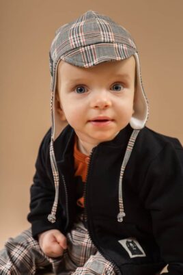 Junge trägt graue Schottenmuster karierte Baby Fliegermütze Hut Kappe mit Schirm Schildmütze - Schwarze Sweatjacke mit Bären Patch Reißverschluss - Braunen Wickelbody Bär von Pinokio - Babyphoto Kinderphoto