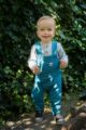 Lachender Junge trägt türkis blaue Latzhose Babyhose mit Tasche & Vehicle Automobile Patch - Baumwollbody blau gestreift mit Holz Knöpfe von Pinokio - Babyphoto Kinderphoto