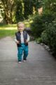 Laufender Junge trägt türkise Babyhose mit Taschen & Knöpfe - Kinder Steppweste schwarz mit Auto-Patch - Blau gestreifter Baby Baumwollbody langarm von Pinokio - Babyphoto Kinderphoto