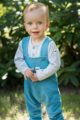Stehender Junge trägt türkise Baby Kinder Latzhose mit Auto Patch & Tasche - Blau gestreiften Polo Langarmbody mit Knöpfe von Pinokio - Babyphoto Kinderphoto