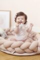 Lachendes Baby mit rosa grau Baby Rassel Holz Beißring Greifling sitzt in hellrosa Baby Nest geflochten mit Spieluhr Sterne von Nordic Coast Company - Babyfoto Kinderfoto