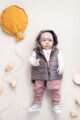 Baby Junge trägt graue Steppweste mit Kapuze - Pumphose mit Taschen & Patch Berge - Beige Kindermütze mit Umschlag aus Baumwolle OEKO TEX von Pinokio - Liegender Junge Babyphoto