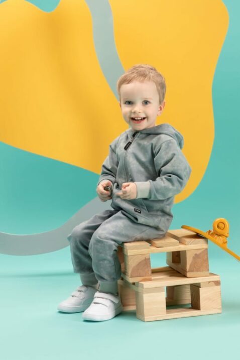 Baby & Kinder BATIK Strampelanzug Overall mit Fuß, Kapuze, FUN Patch & Reißverschluss in Mint von Pinokio - Kinderfoto sitzender lachender Junge
