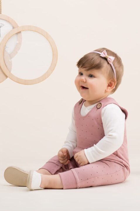 Lachendes Mädchen trägt Baby Latzhose Einteiler mit Punkte, Falten & Knöpfe in Rosa - Weißes Langarmshirt von PINOKIO - Babyfoto Kinderhose Outfit