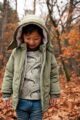 Junge trägt grüne warm gefütterte Baby & Kinder Winterjacke mit Kapuze, Taschen & Reißverschluss von Koko Noko - Kinderfoto stehender Junge mit Winter Kinderjacke im Herbst