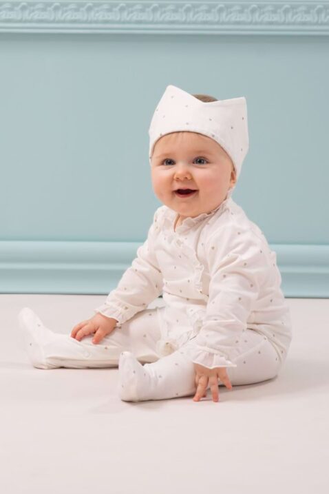 Sitzendes Baby trägt weißen Schlafoverall mit Füßen, langen Ärmeln, Rüschen & Herze gemustert in Ecru Weiß von Pinokio - Babyfoto langarm Einteiler Strampler festliche Kleidung für Babys