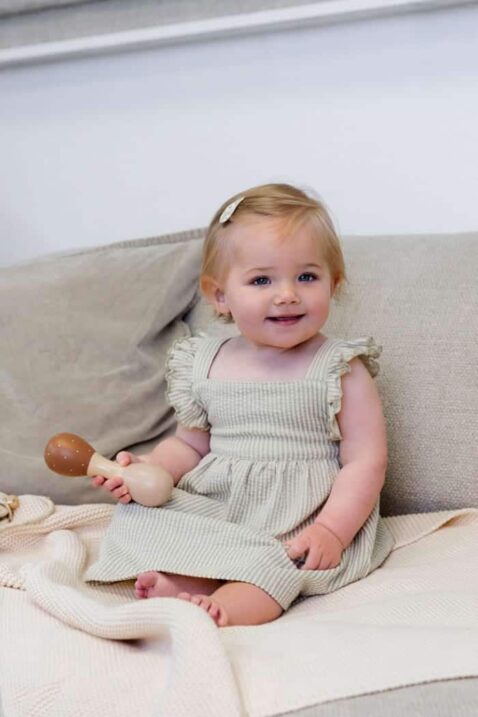 Sommerkleid midi lang mit hellgrünen weißen Streifen, Rüschen an Schulterträger für Babys & Kinder von Dirkje - Kinderfoto lachends Mädchen auf Sofa mit weit geschnittenem Musselin-Kleid