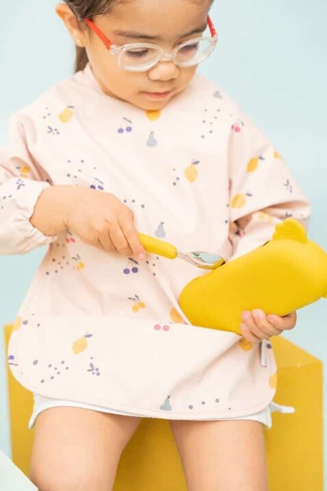 Ärmellätzchen für Babys & Kleinkinder mit Auffangschale, elastische Ärmelabschlüsse, Zitronen, Kirschen & Birnen gemustert in Rosa von THE COTTON CLOUD - Kinderfoto Mädchen trägt wasserdichtes & nachhaltiges Langarm-Lätzchen mit Früchte Motiven & Klettverschluss