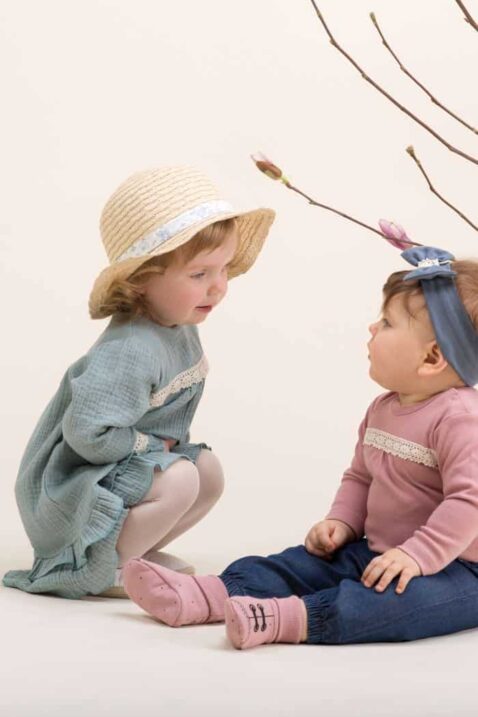 Zwei sitzende Mädchen tragen langärmelige PINOKIO Musselinkleider für Babys und Kinder aus grüner Baumwolle mit feiner Häkelspitze – leichte, sommerliche Babykleider & Kinderkleider für Mädchen in natürlichem Look
