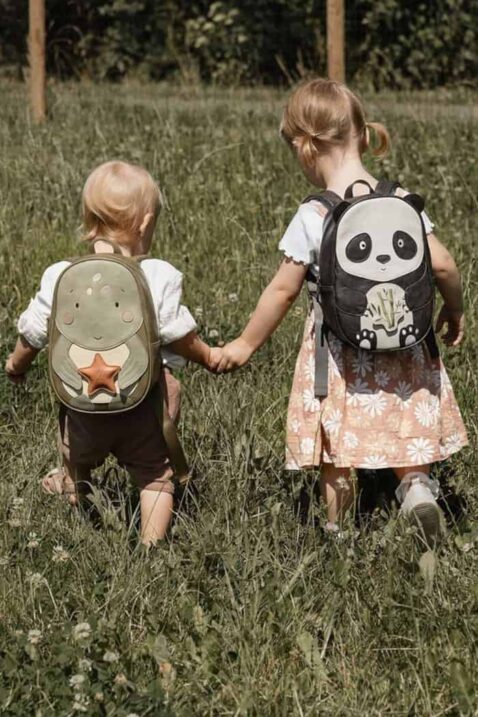 Baby & Kinder Mädchenrucksäcke aus veganem, recyceltem Leder Vintage Retro von LITTLE WHO - Kinderfoto blondes großes Mädchen mit Rucksack Panda Suki in Schwarz & kleines blondes Mädchen mit Rucksack Schildkröte Marta laufen auf einer Wiese